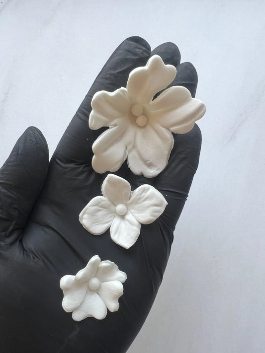 Close-up of white edible fondant flowers in different sizes held in hand for cake decorating