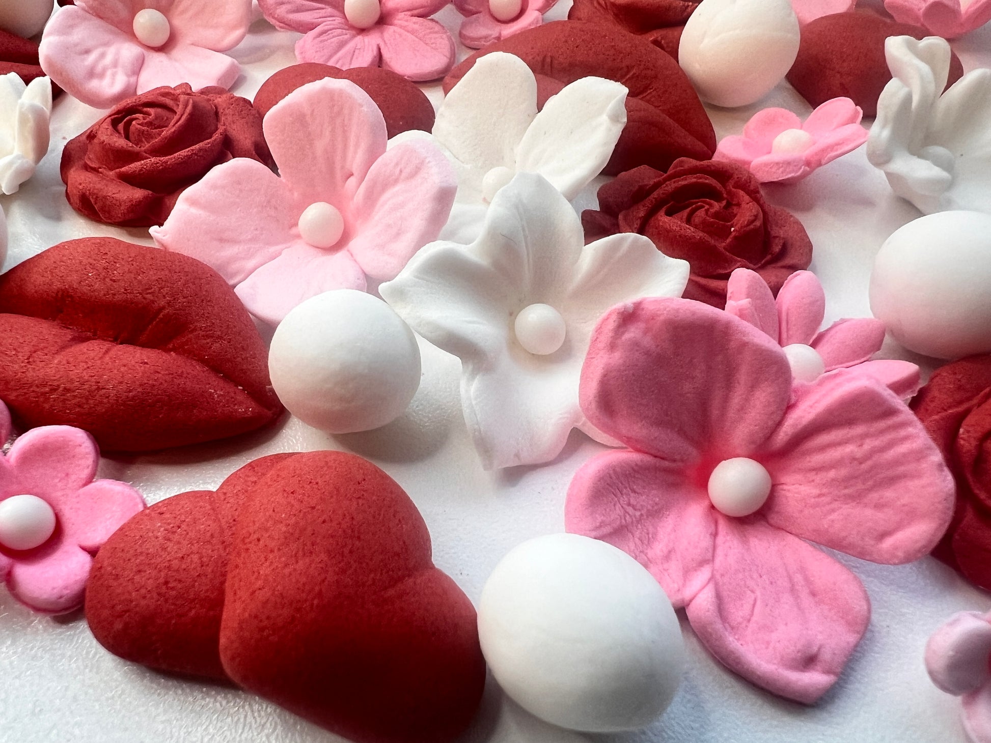Decorative flowers and hearts made of fondant in red, pink, and white on a light background.