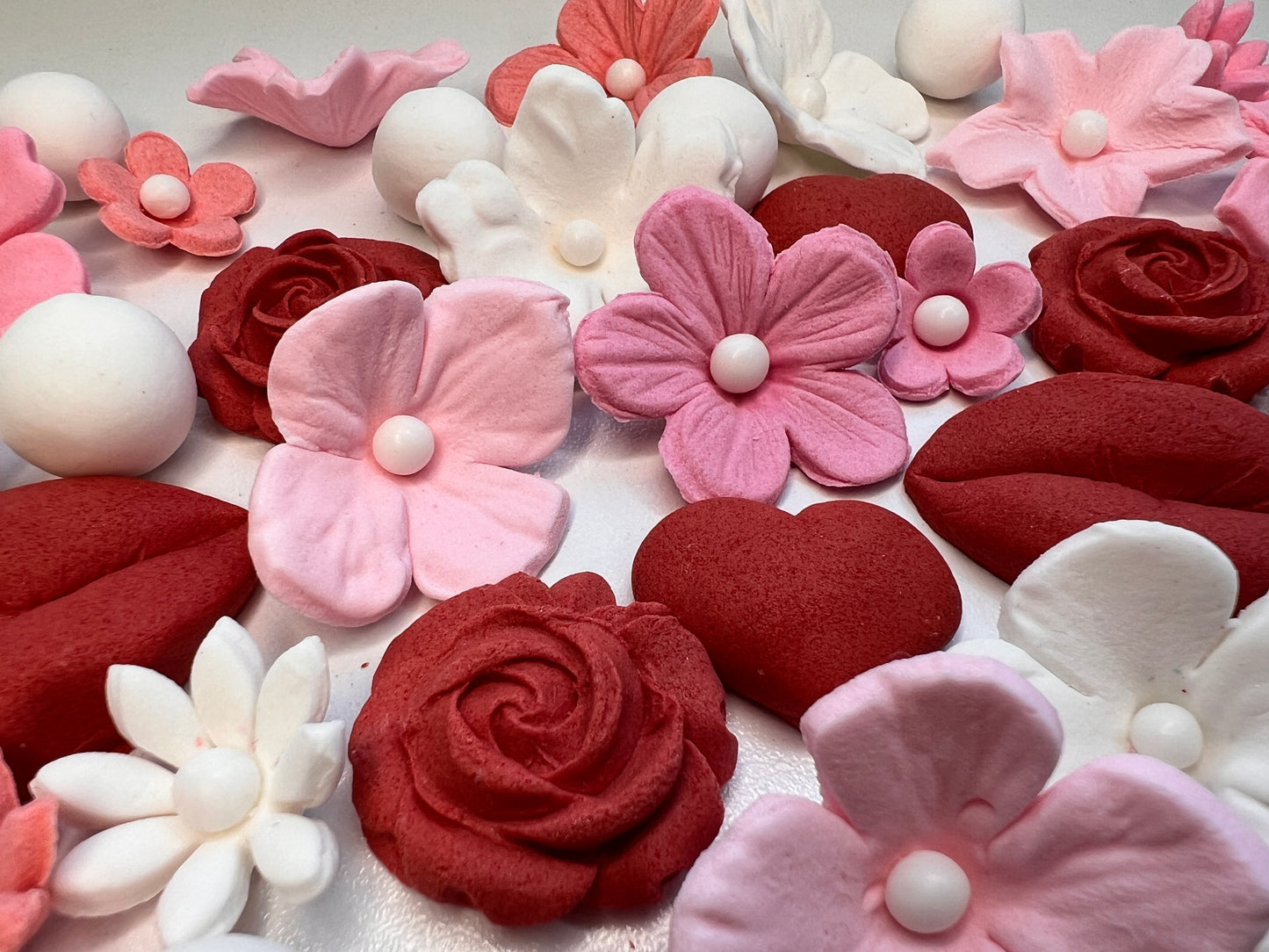 Assorted pink, red, and white floral and heart-shaped fondant decorations on a light background.