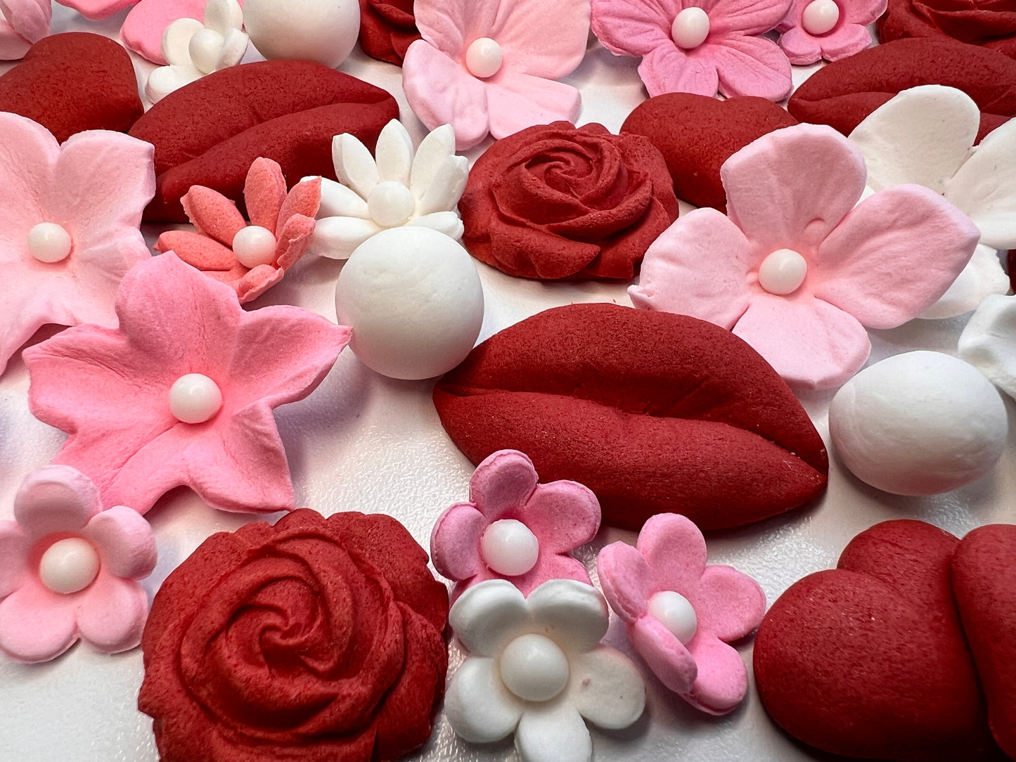 Close-up of red, pink, and white floral and heart-shaped decorations made of fondant. .