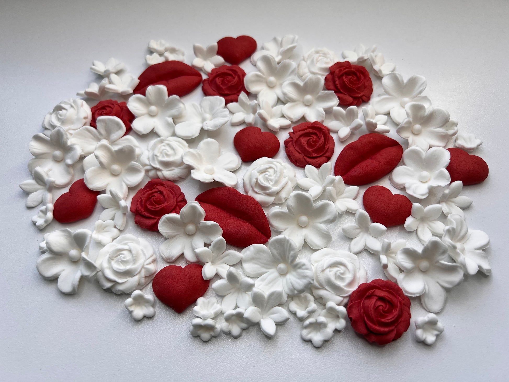 Heart-shaped fondant arrangement of red and white floral and heart-shaped decorations on a light gray background