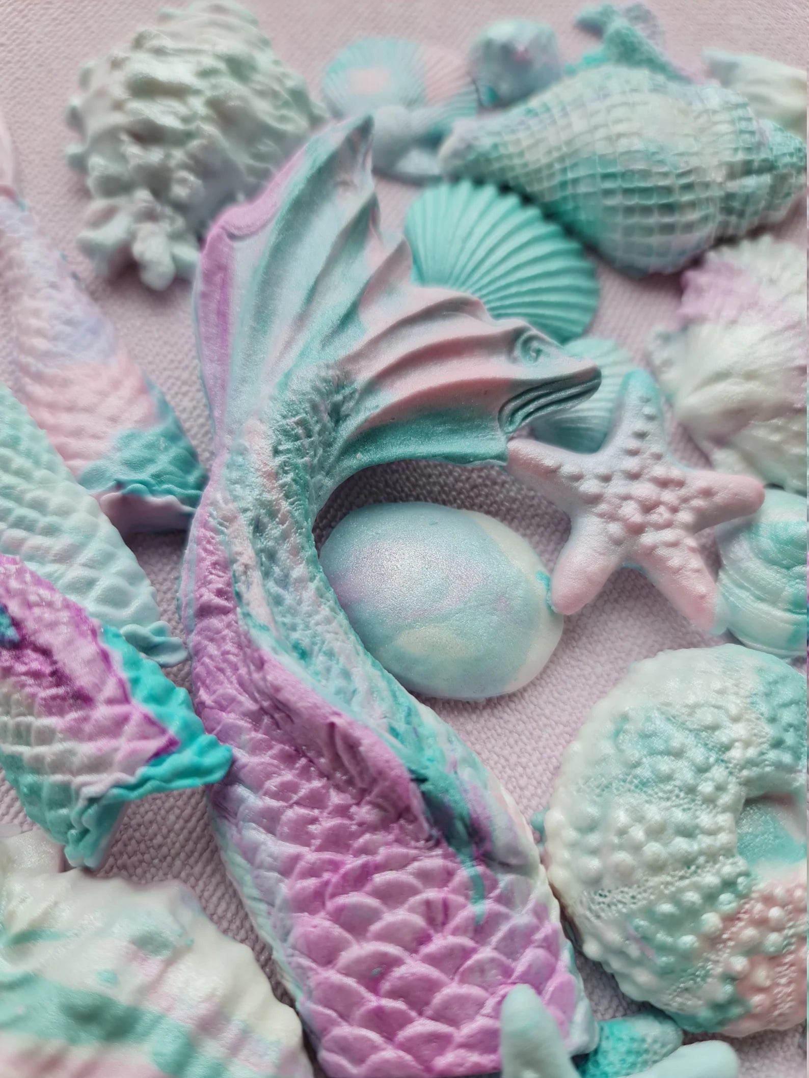 Pastel-colored sea-themed fondant decorations including shells and a mermaid tail on a pink background.