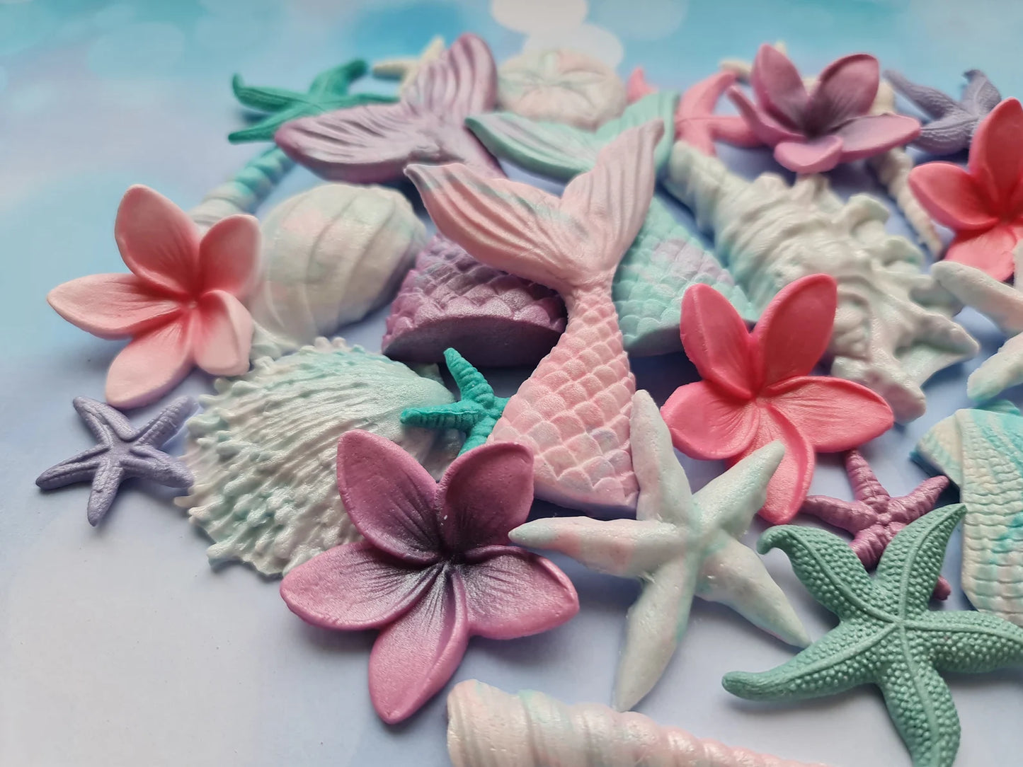 Colorful sea-themed fondant 
decorations including mermaid tails, flowers, and shells on a light background.