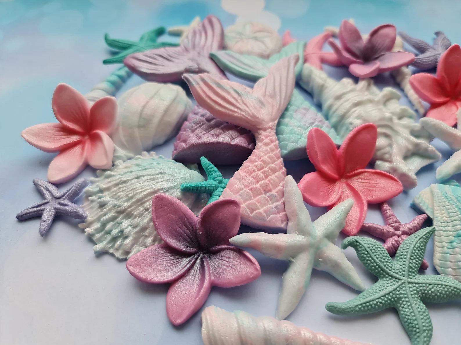 Colorful sea-themed fondant 
decorations including mermaid tails, flowers, and shells on a light background.