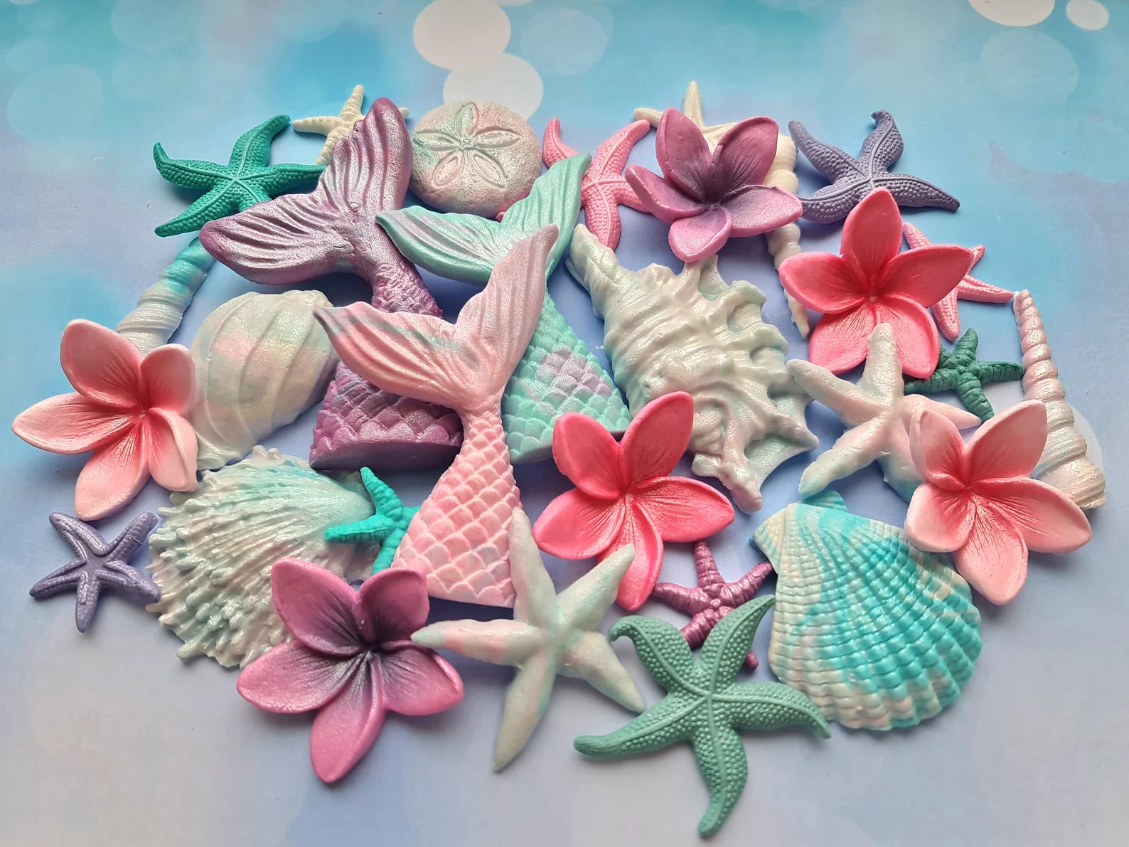 Colorful sea-themed sugar decorations including mermaid tails, flowers, and starfish on a light blue background.
