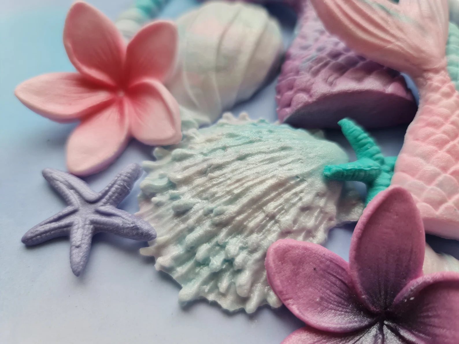 Colorful sea-themed sugar decorations including plumeria and shells on a light blue background