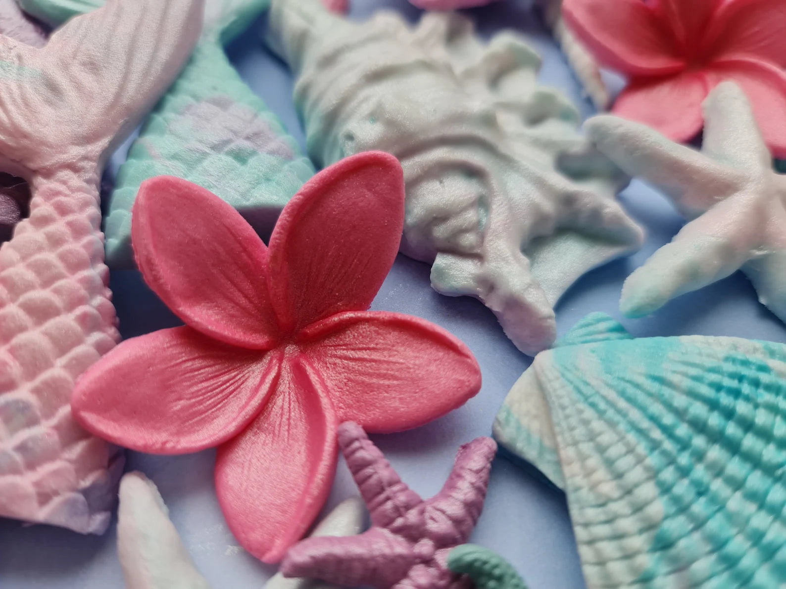 Colorful sugar shaped like seashells and a flower on a light purple background