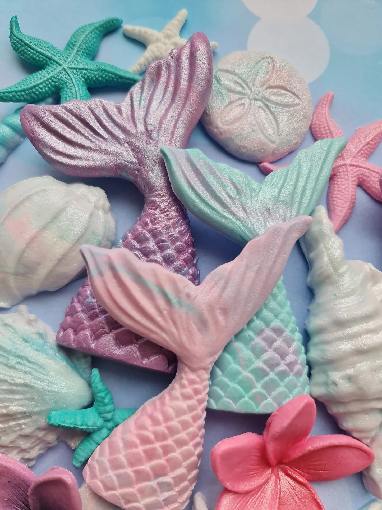 Colorful mermaid tail sugar decorations on a blue background with starfish and sand dollar decorations.