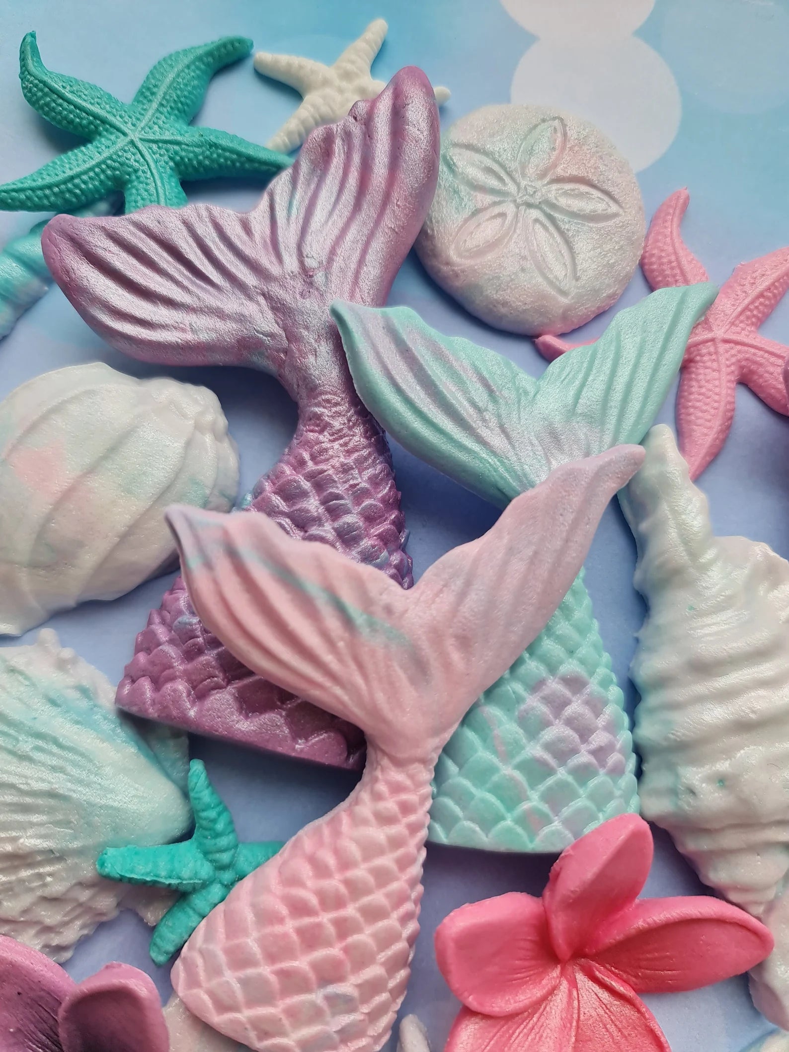 Colorful mermaid tail sugar decorations on a blue background with starfish and sand dollar decorations.
