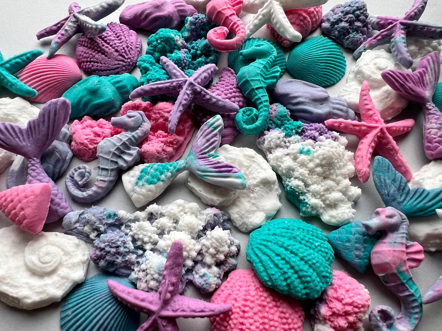 Colorful sea-themed sugar decorations including mermaid tails, seashells, and starfish on a white background.