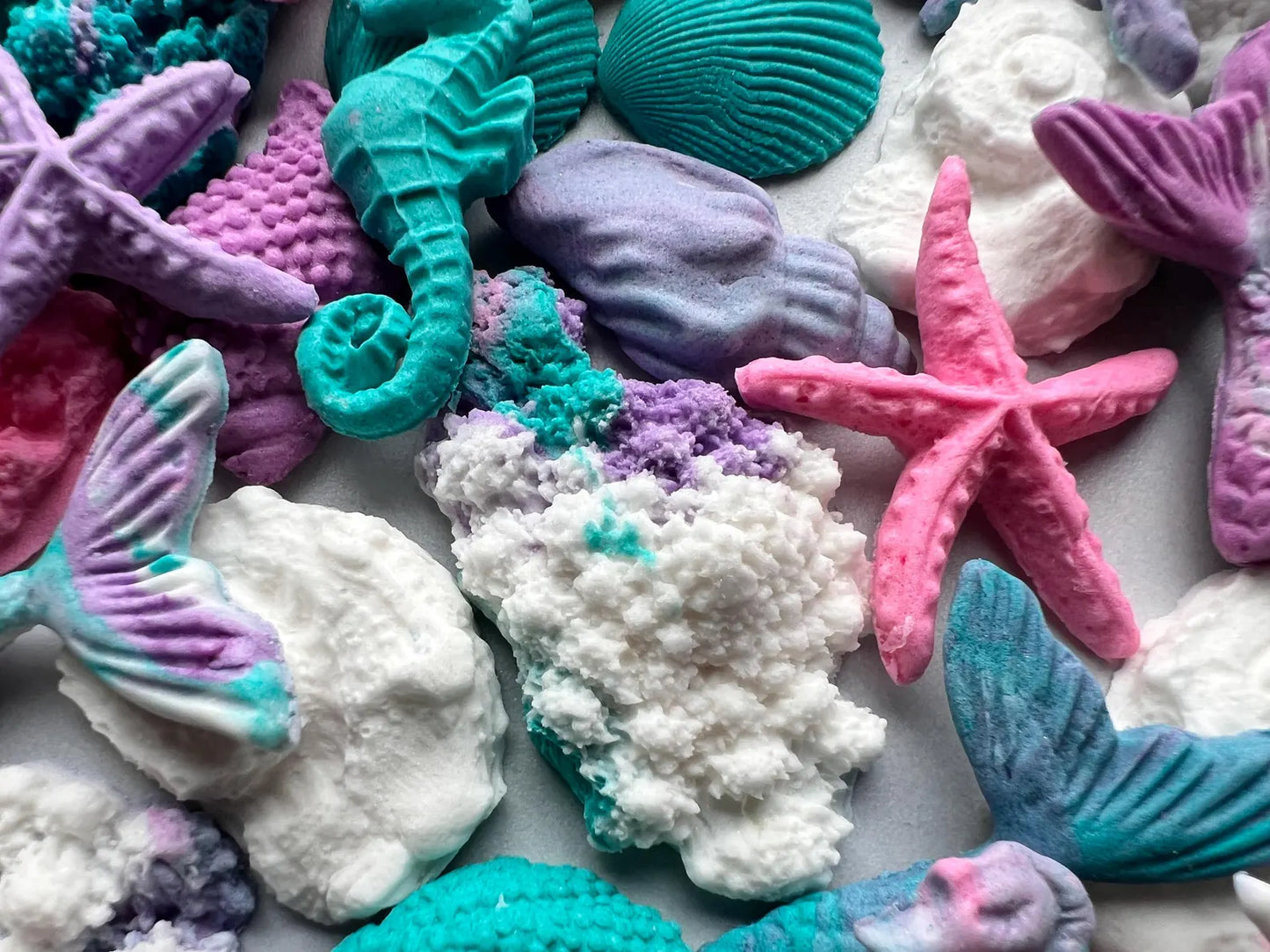 Colorful sea-themed fondant decorations including mermaid tails, seahorses, and starfish on a white background.