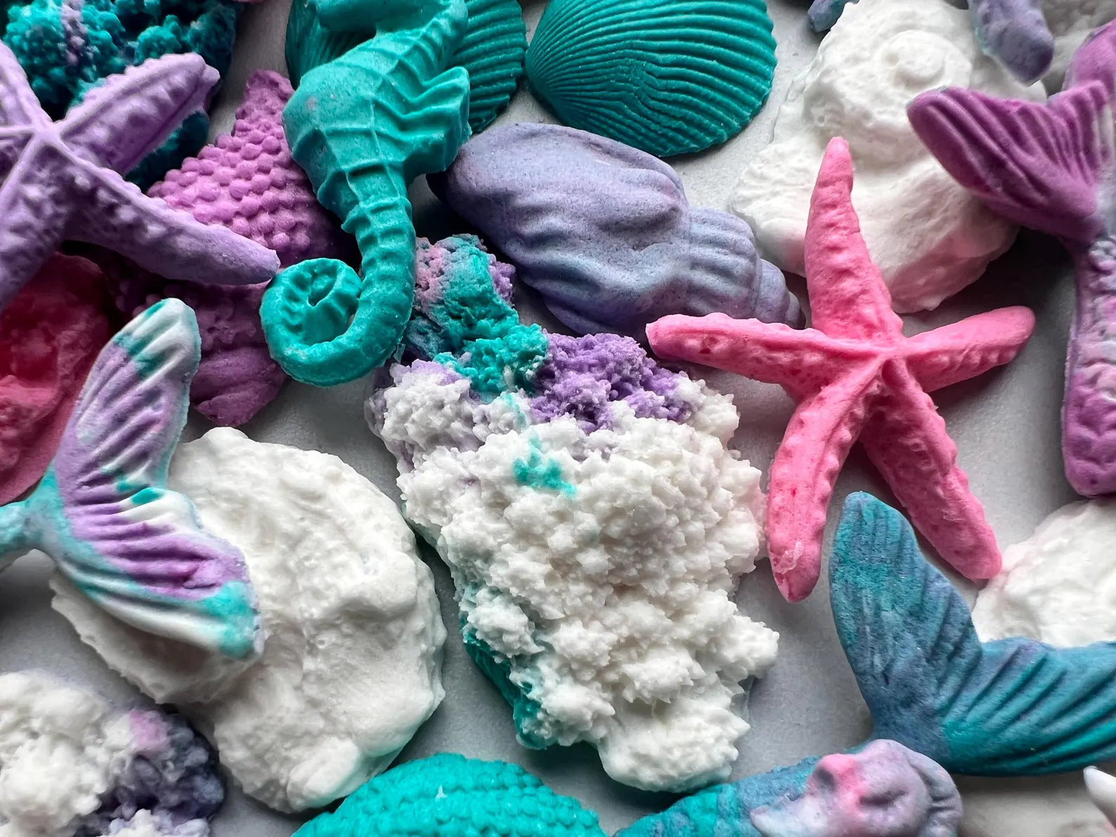 Colorful sea-themed fondant decorations including mermaid tails, seahorses, and starfish on a white background.