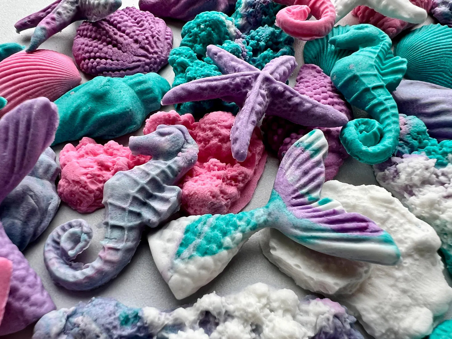 Colorful sea-themed fondant decorations including seashells, starfish, and mermaid tails on a white background.