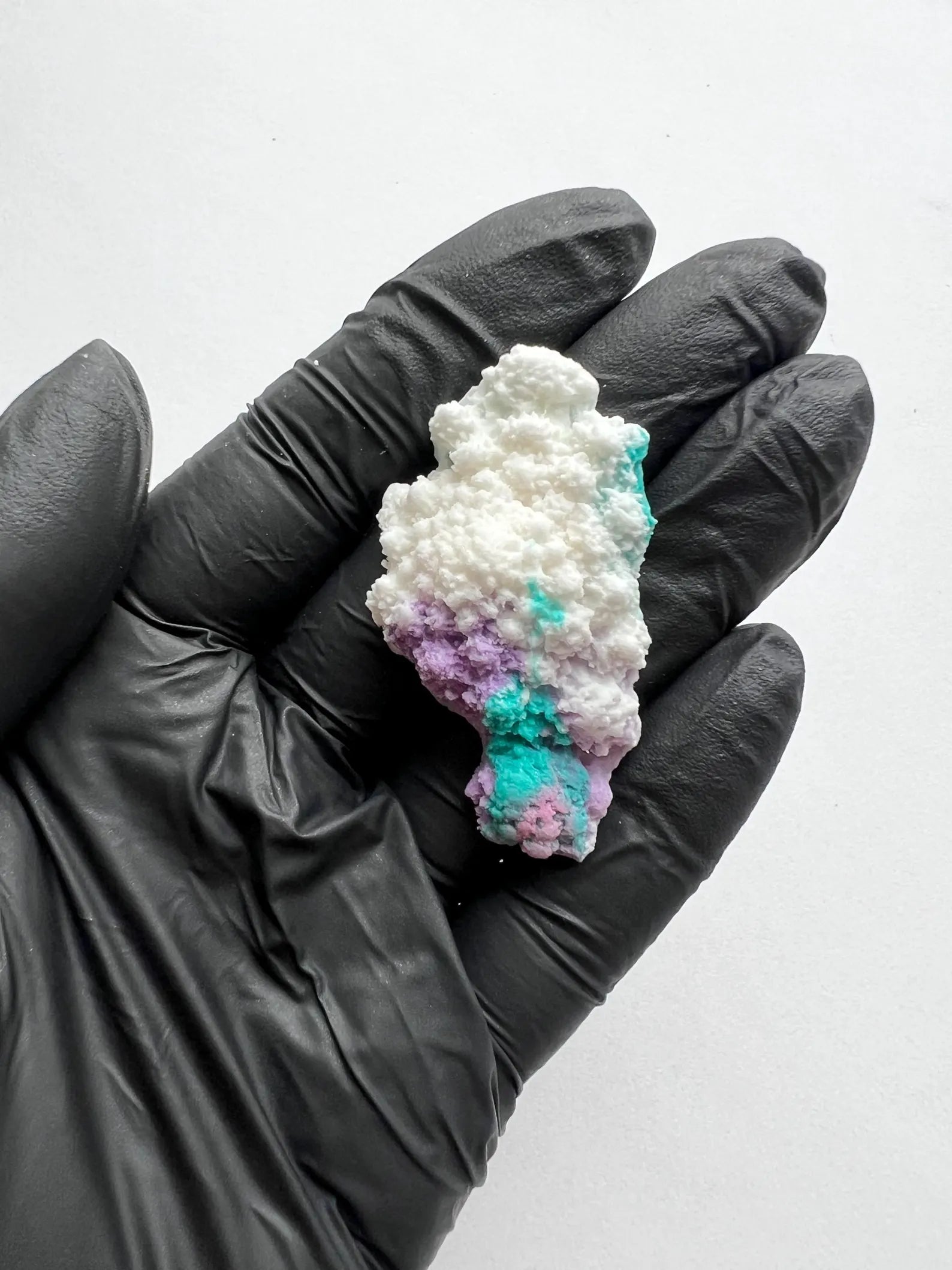 Multicolored fondant coral held in a black-gloved hand against a white background