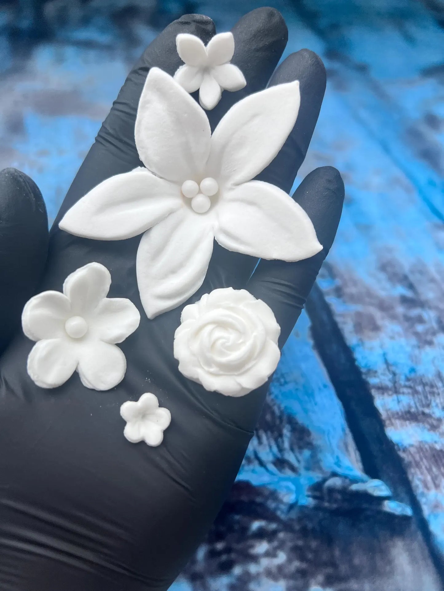 Close-up of white edible fondant flower decorations in assorted shapes held in hand for cake decorating