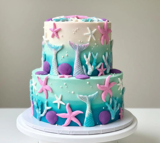Two-tiered mermaid-themed cake with starfish, shells, and mermaid tails on a plain background.