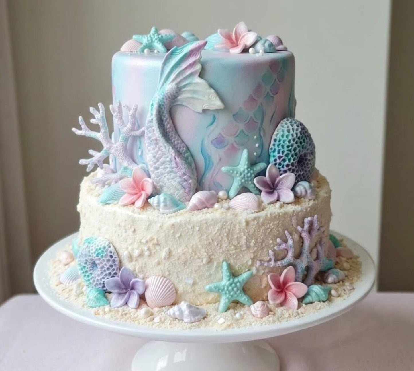 Pastel under the sea themed cake decorated with edible mermaid tail, shells, starfish, coral and sea-inspired sugar decorations.