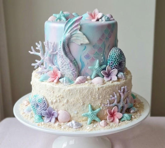 Pastel under the sea themed cake decorated with edible mermaid tail, shells, starfish, coral and sea-inspired sugar decorations.