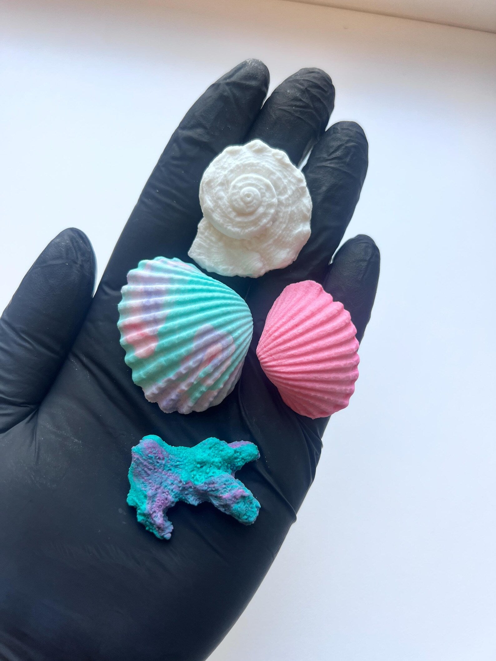 Close-up of edible sea life cake decorations including pastel shells, coral and spiral shell details, shown on a gloved hand for size reference