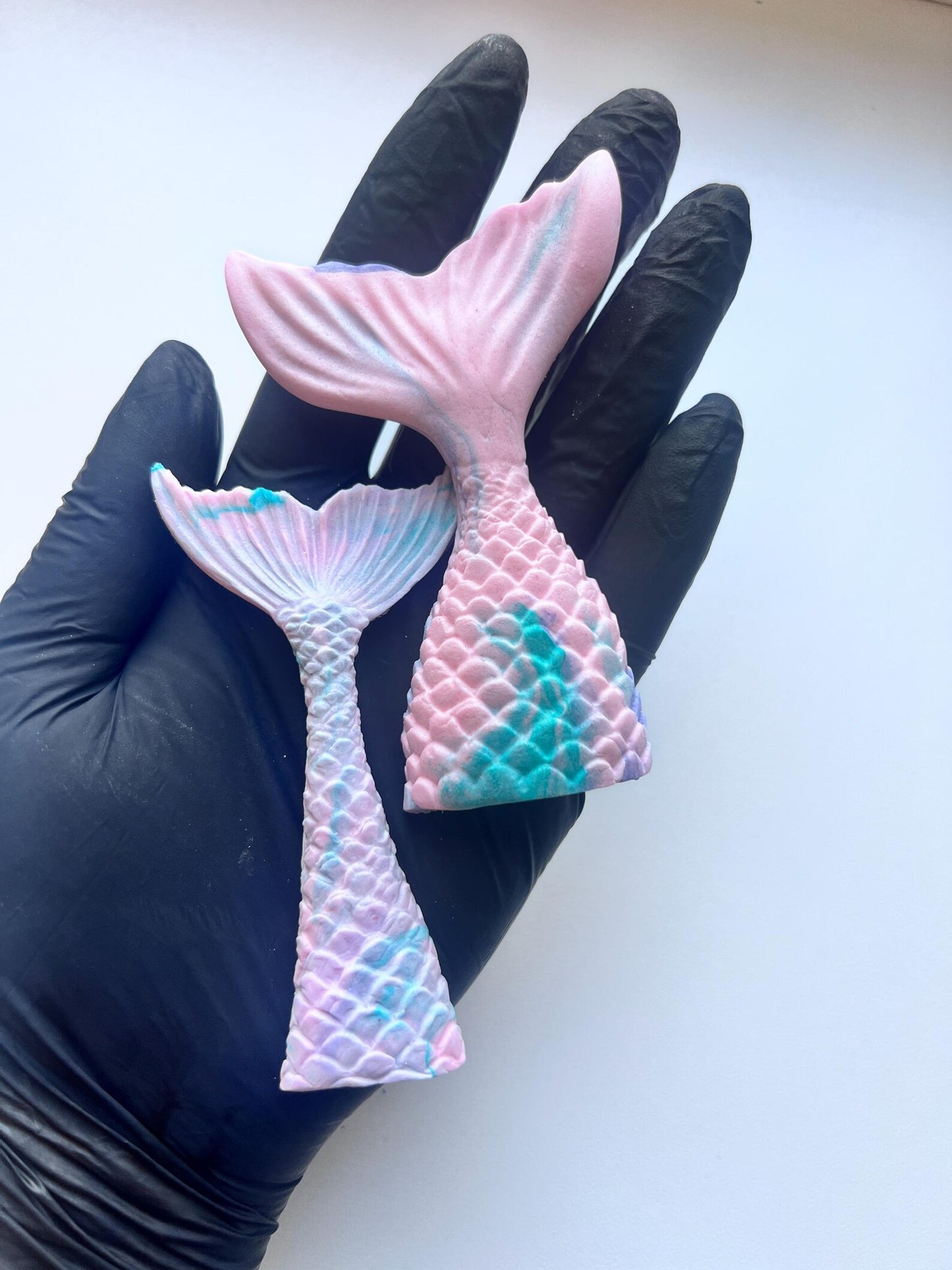 Edible mermaid tail cake decorations in pastel pink, purple and teal colors, shown on hand for size reference