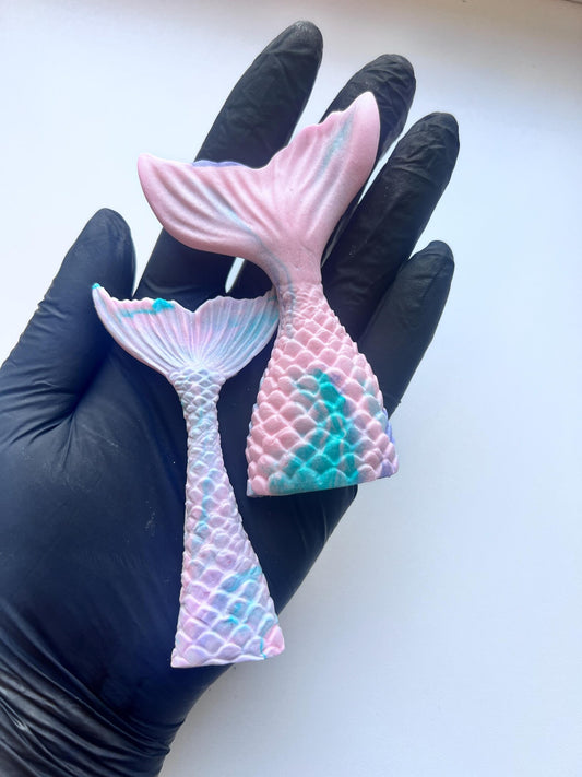 Edible mermaid tail cake decorations in pastel pink, purple and teal colors, shown on hand for size reference
