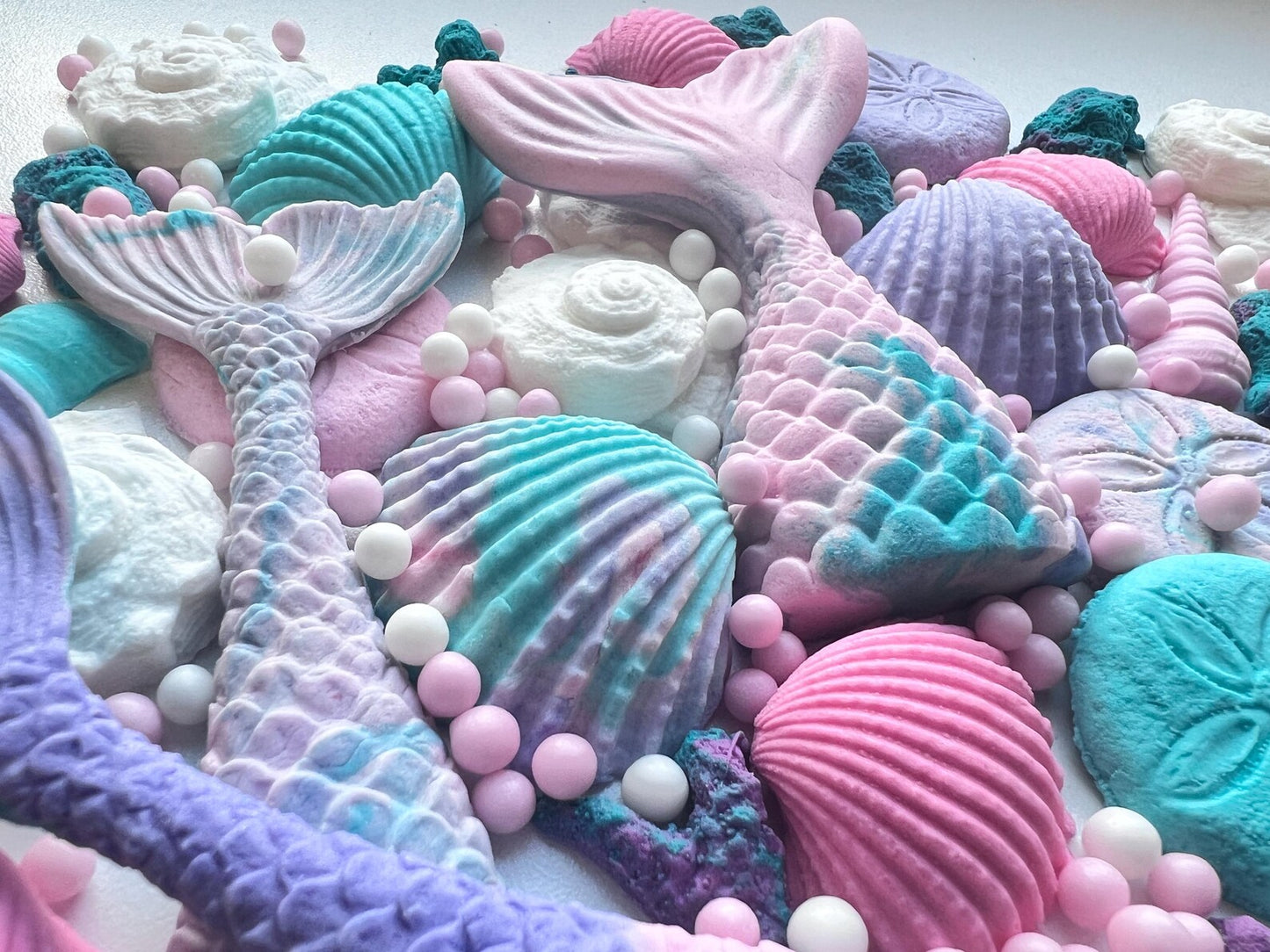 Close-up of pastel edible sea-themed cake decorations featuring mermaid tails, shells, coral and sugar pearls.