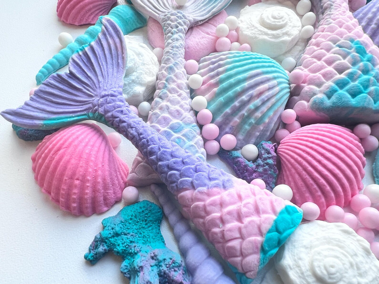 Close-up of edible mermaid tail cake decorations with pastel shells, coral pieces and sugar pearls in ocean colors.