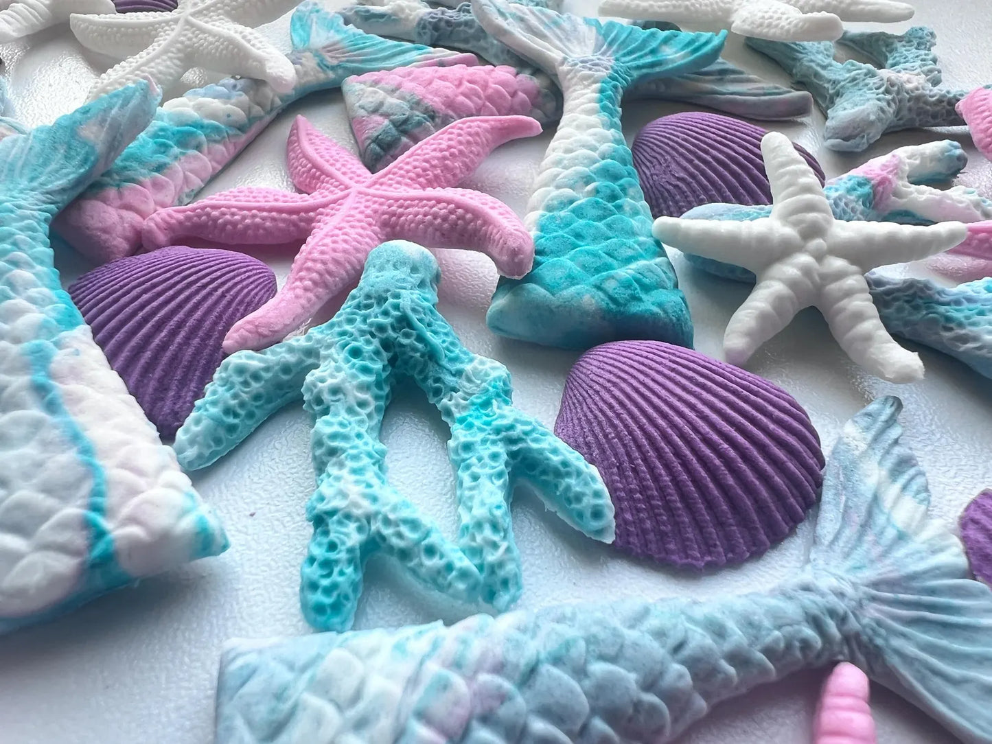 Colorful sugar sea-themed decorations including mermaid tails, starfish, and seashells on a white background.