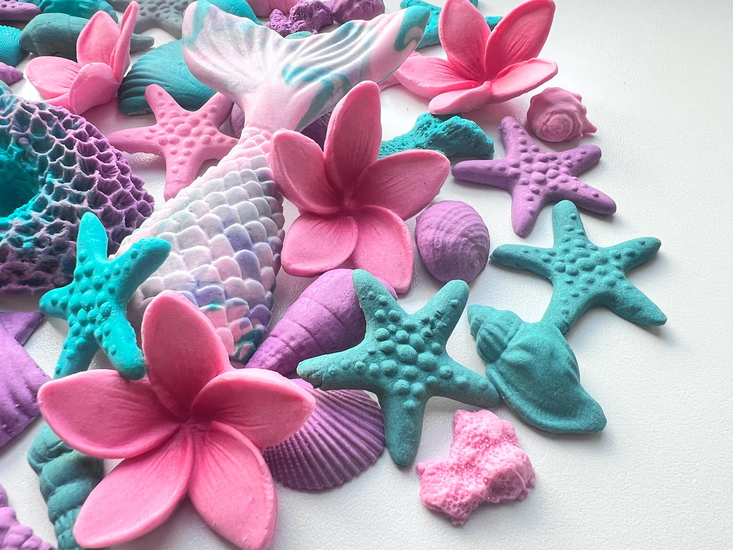 Colorful sea-themed sugar decorations including flowers, mermaid tails, and starfish on a white background.
