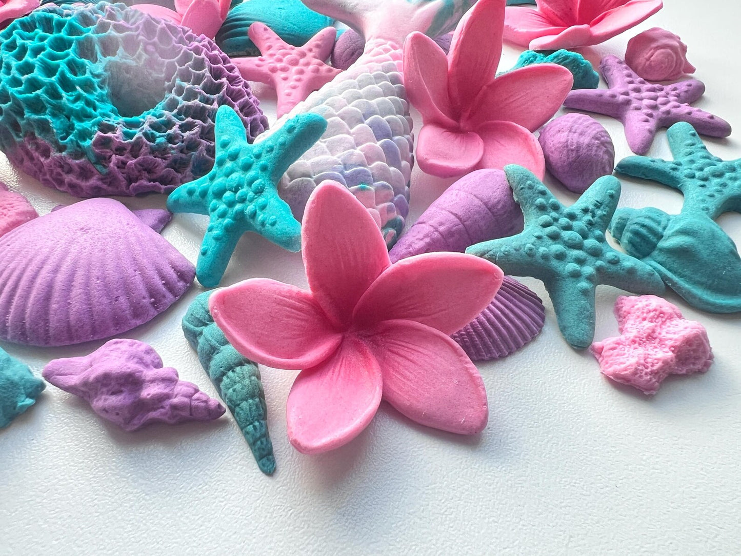 Colorful sea-themed fondant decorations including starfish, shells, and plumerias on a white background