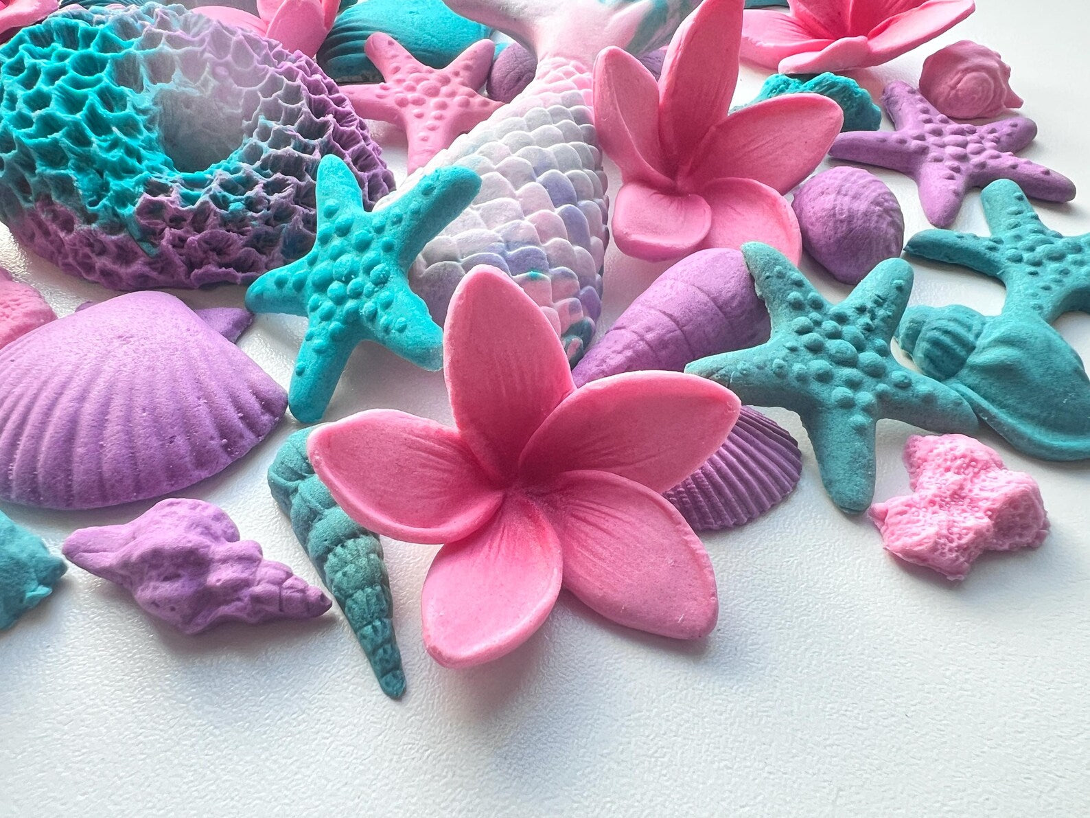 Colorful sea-themed fondant decorations including starfish, shells, and plumerias on a white background