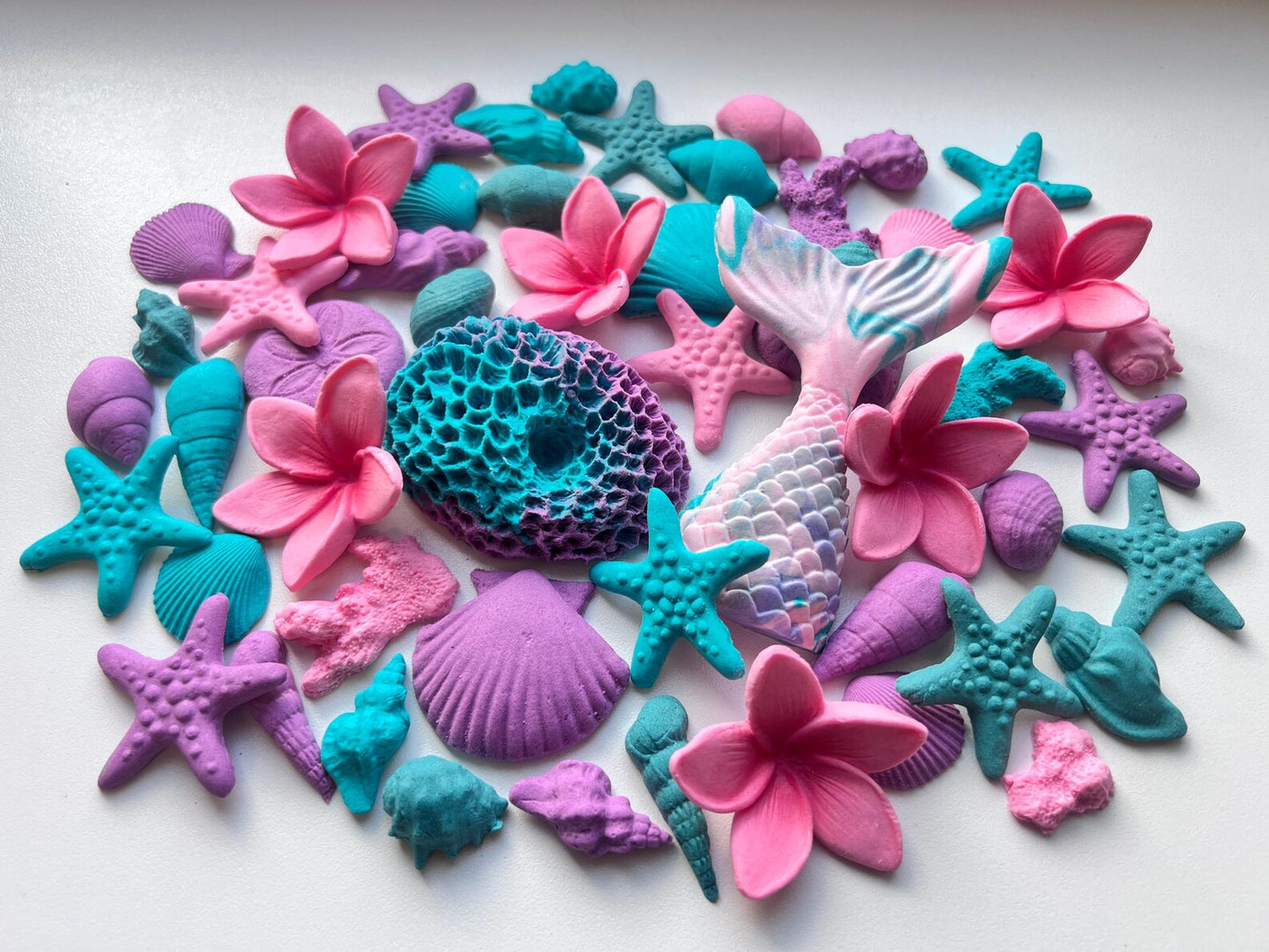 Colorful sea-themed sugar decorations including plumeria, starfishes, and mermaid figures on a white background.