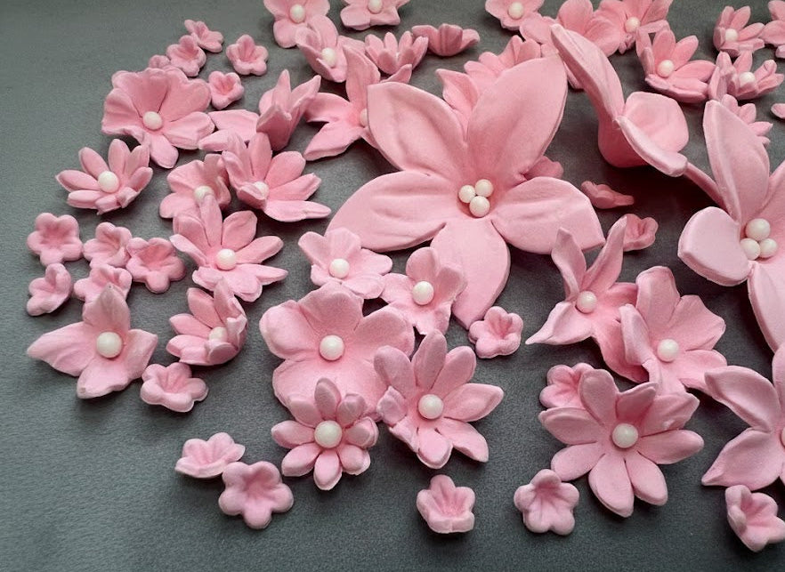 Pink fondant floral decorations with pearl centers on a dark background