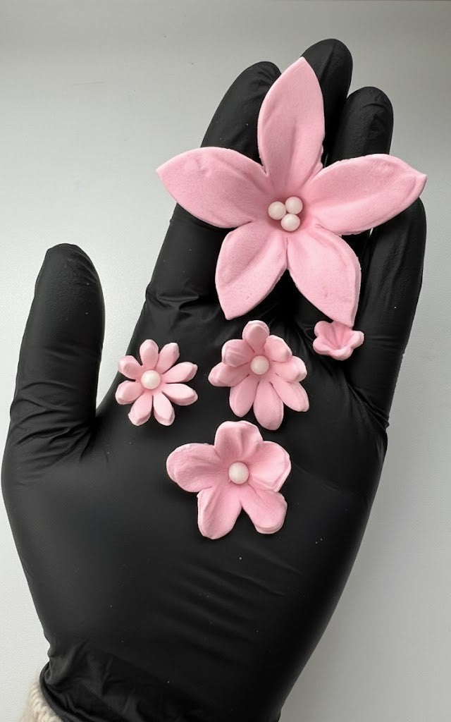 Pink fondant flower held in a black gloved hand